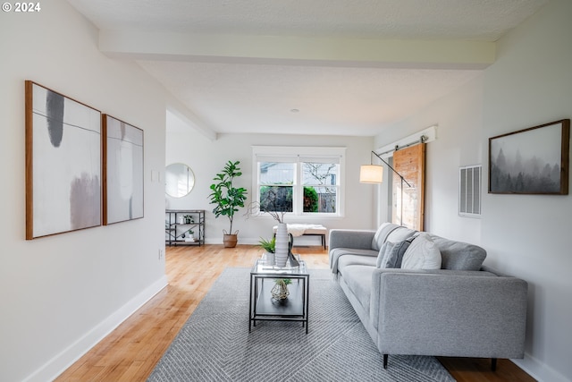 living room featuring beamed ceiling, a barn door, light hardwood / wood-style floors, and a textured ceiling