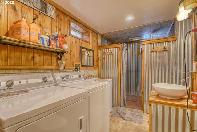 clothes washing area with laundry area, wood walls, washing machine and dryer, a sink, and light tile patterned floors