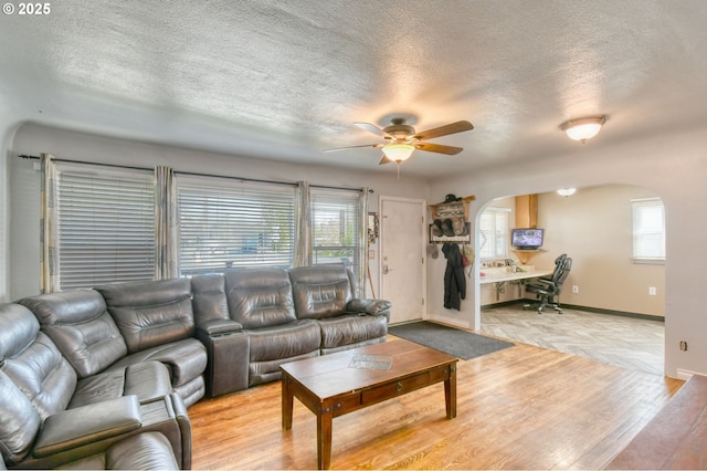 living area featuring arched walkways, a textured ceiling, ceiling fan, and a wealth of natural light