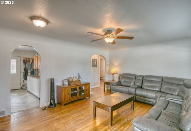 living area featuring light wood-style floors, arched walkways, baseboards, and a ceiling fan