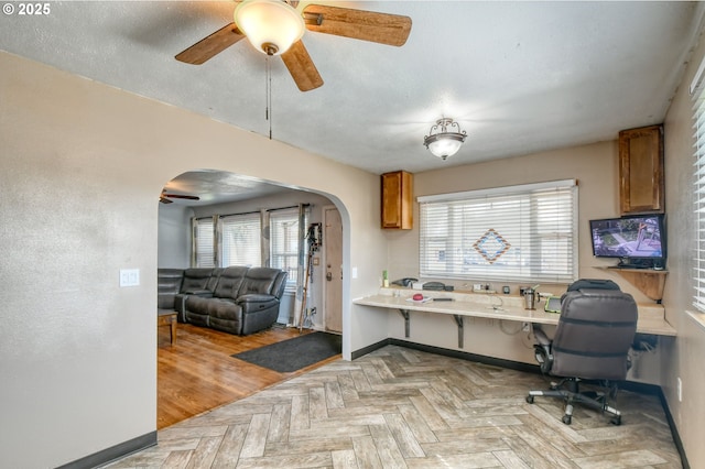 office featuring baseboards, arched walkways, a textured ceiling, and a ceiling fan