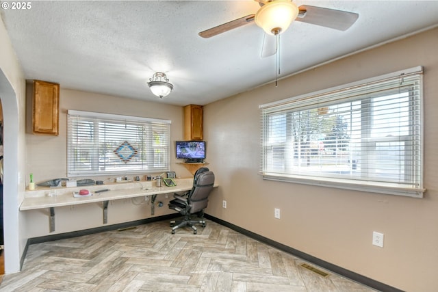 home office with a ceiling fan, a textured ceiling, visible vents, arched walkways, and baseboards