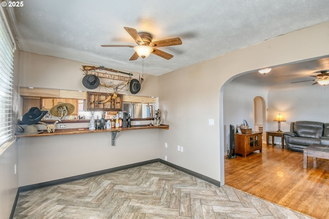 interior space with a ceiling fan, arched walkways, a wealth of natural light, and baseboards