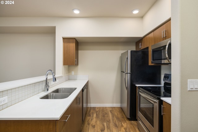 kitchen featuring dark wood finished floors, decorative backsplash, brown cabinets, stainless steel appliances, and a sink