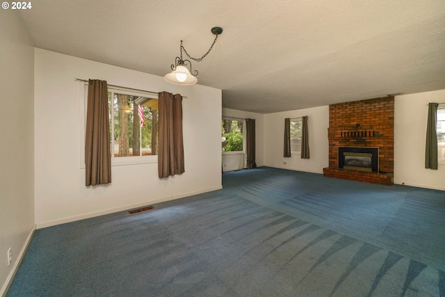 unfurnished living room with dark colored carpet, a textured ceiling, and a brick fireplace