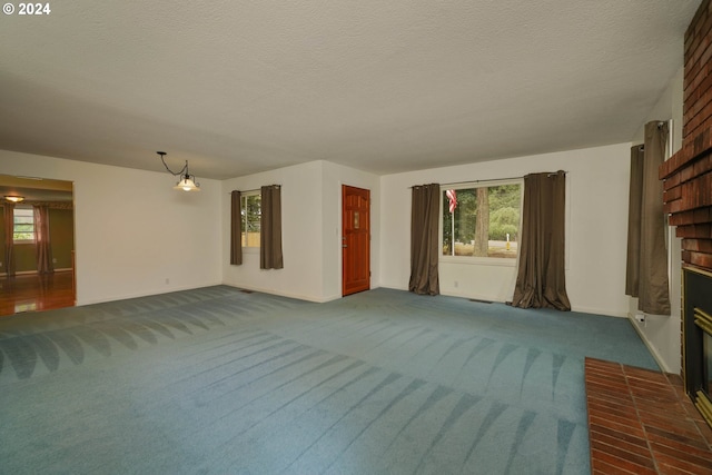 unfurnished living room with dark carpet, a brick fireplace, a wealth of natural light, and a textured ceiling