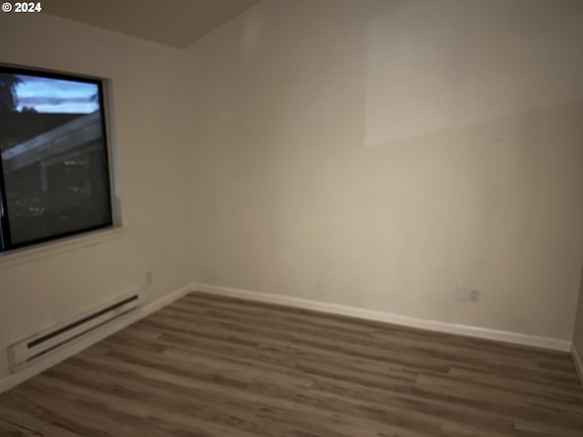 unfurnished room with dark wood-type flooring and a baseboard heating unit