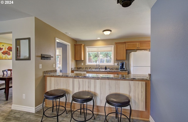 kitchen featuring a kitchen bar, white fridge, dark stone countertops, sink, and kitchen peninsula