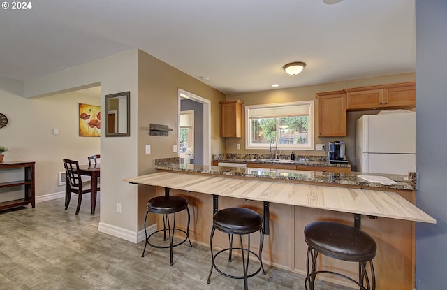 kitchen featuring kitchen peninsula, a kitchen breakfast bar, sink, white refrigerator, and light hardwood / wood-style floors