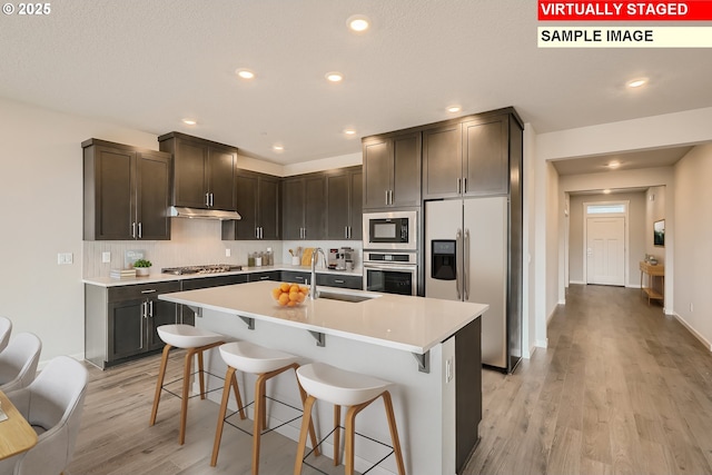 kitchen featuring appliances with stainless steel finishes, a kitchen breakfast bar, light countertops, light wood-type flooring, and a sink