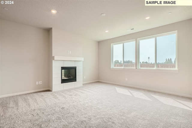 unfurnished living room featuring light colored carpet, a textured ceiling, and a tile fireplace