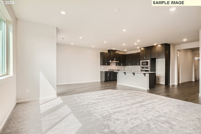 kitchen featuring a kitchen bar, a kitchen island with sink, built in microwave, sink, and oven