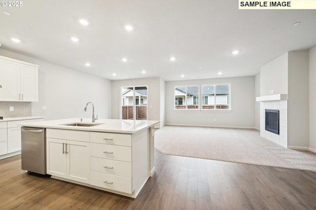 kitchen featuring a tiled fireplace, light countertops, a sink, and wood finished floors