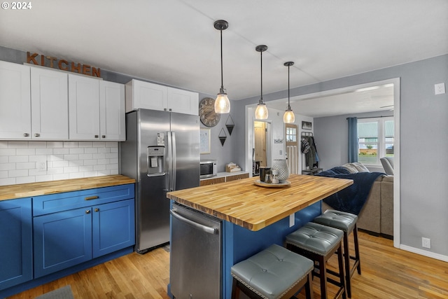 kitchen featuring a breakfast bar area, white cabinetry, stainless steel appliances, blue cabinets, and butcher block countertops