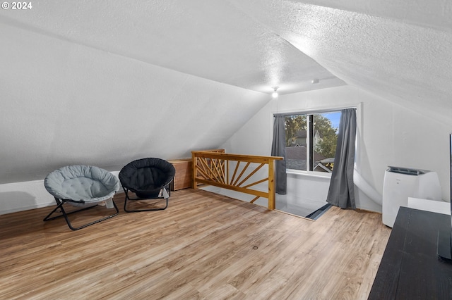 additional living space with vaulted ceiling, a textured ceiling, and light wood-style floors