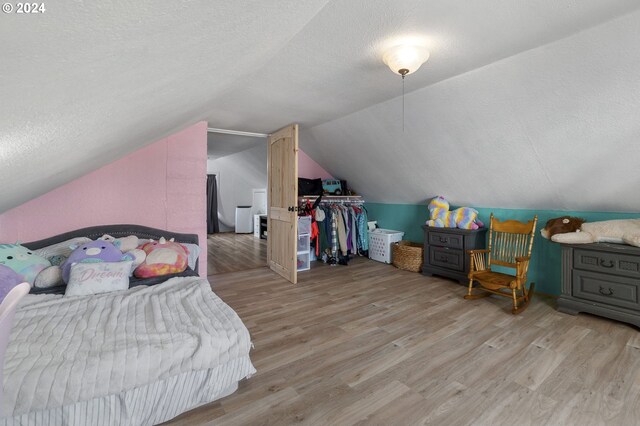 bedroom featuring lofted ceiling, a textured ceiling, and light wood-type flooring