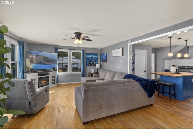 living room with ceiling fan, light wood-type flooring, and a glass covered fireplace