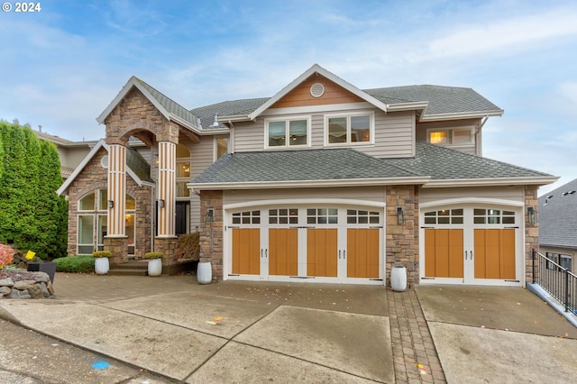 view of front of property with stone siding, concrete driveway, roof with shingles, and a garage