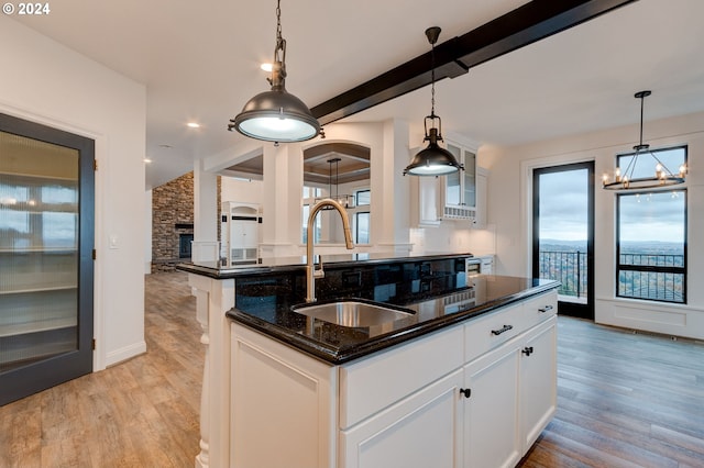 kitchen with a sink, light wood-style floors, dark stone countertops, white cabinets, and beam ceiling