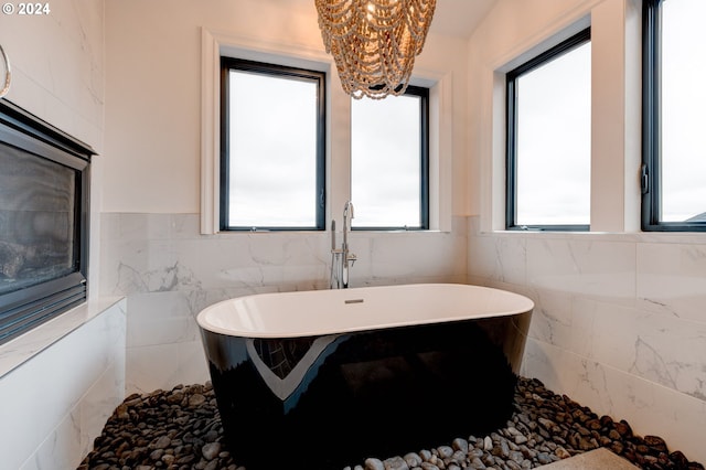 bathroom featuring tile walls, a chandelier, plenty of natural light, a freestanding tub, and a wainscoted wall
