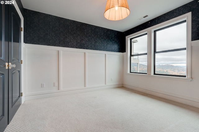 carpeted empty room with wainscoting, wallpapered walls, and a decorative wall