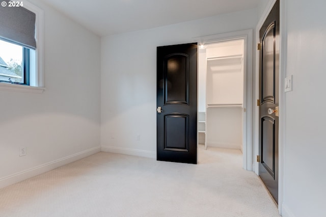 unfurnished bedroom with a spacious closet, light carpet, and a closet