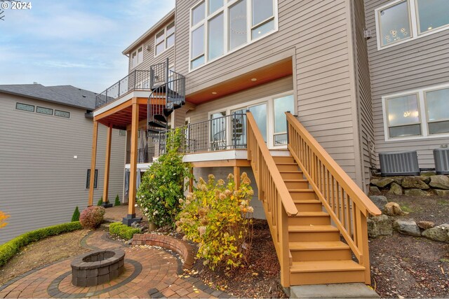 rear view of property featuring a deck, a patio, central air condition unit, and an outdoor fire pit