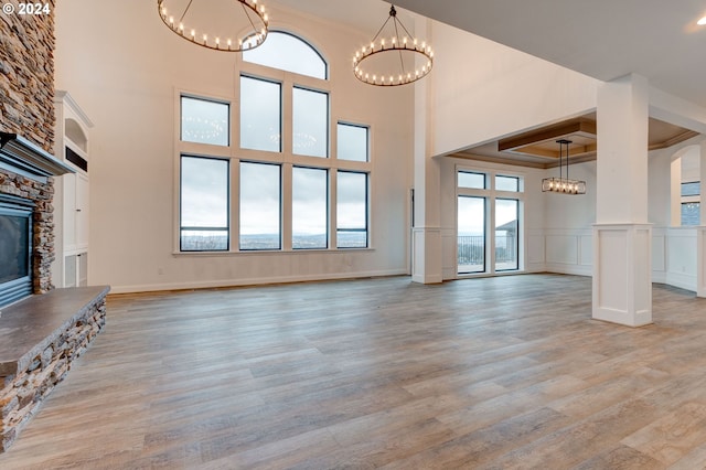 unfurnished living room featuring a high ceiling, a stone fireplace, plenty of natural light, and light hardwood / wood-style flooring