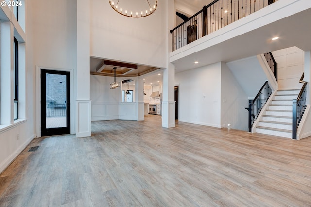 unfurnished living room featuring a chandelier, a towering ceiling, stairway, wood finished floors, and a decorative wall