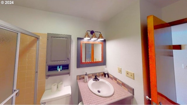 full bathroom featuring a shower with shower door, vanity, and toilet