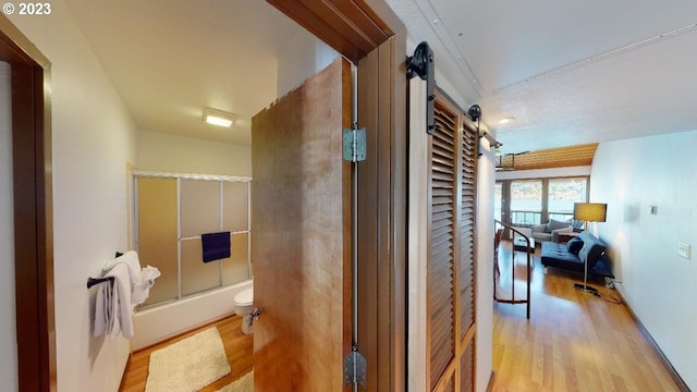 interior space with combined bath / shower with glass door, toilet, and wood finished floors