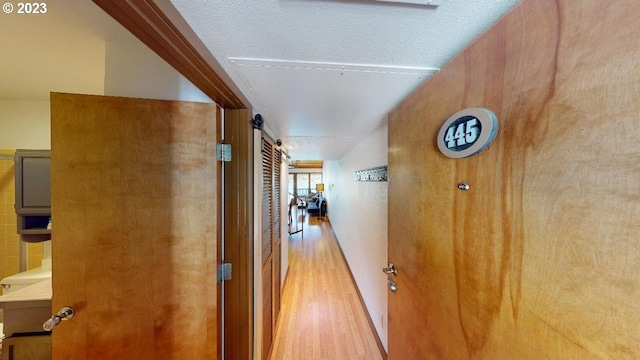 hall featuring light wood finished floors, a barn door, and a textured ceiling