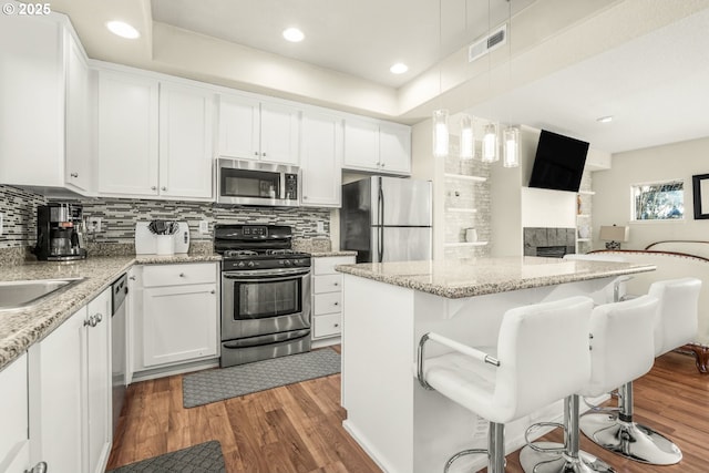 kitchen featuring pendant lighting, a breakfast bar, dark wood-type flooring, appliances with stainless steel finishes, and white cabinetry