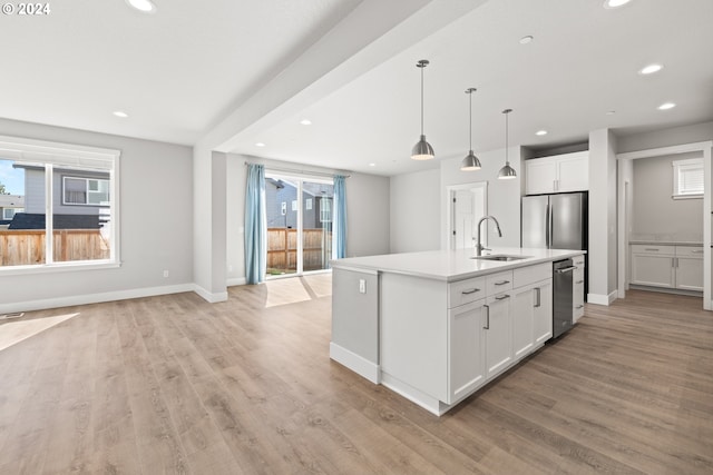 kitchen featuring an island with sink, sink, white cabinetry, stainless steel appliances, and light wood-type flooring