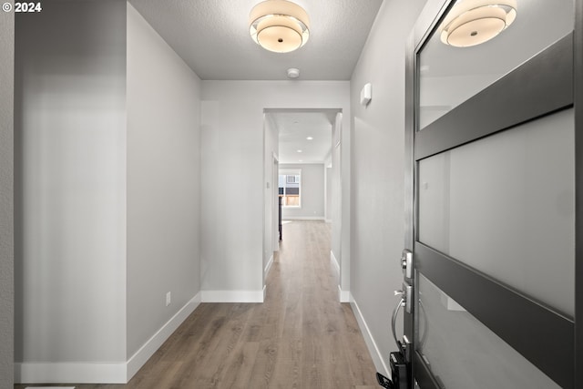 hallway with a textured ceiling and light hardwood / wood-style floors