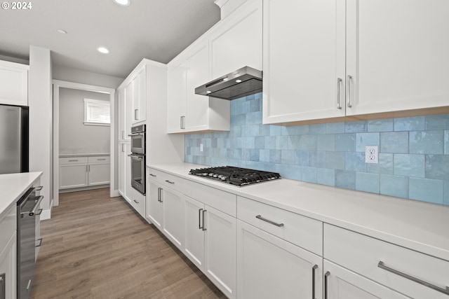 kitchen featuring ventilation hood, white cabinets, light hardwood / wood-style flooring, decorative backsplash, and stainless steel appliances