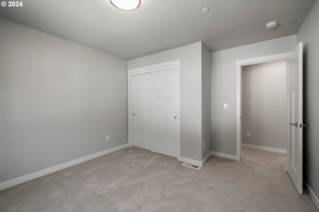 unfurnished bedroom with light colored carpet, a textured ceiling, and a closet