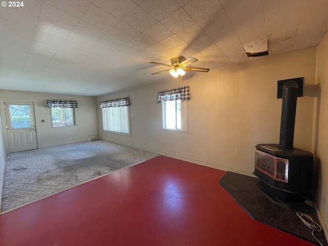 unfurnished living room featuring a wood stove, ceiling fan, and carpet floors