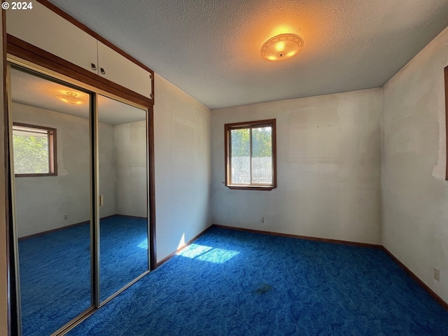 unfurnished bedroom featuring multiple windows, a textured ceiling, dark colored carpet, and a closet