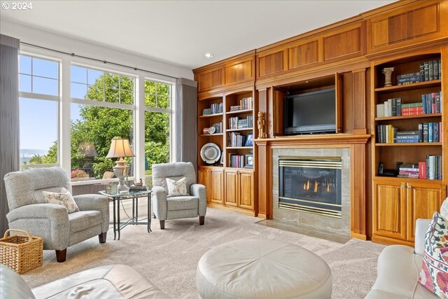 living area featuring light colored carpet, built in shelves, and a premium fireplace