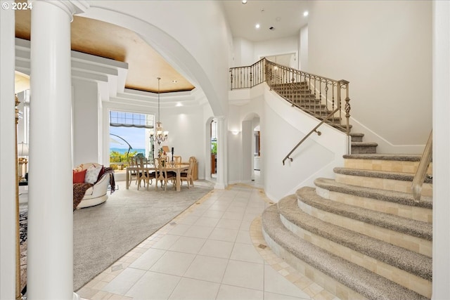 carpeted entryway with an inviting chandelier, a high ceiling, a raised ceiling, and ornate columns