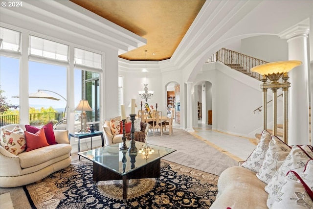 living room featuring a tray ceiling, decorative columns, a high ceiling, an inviting chandelier, and crown molding