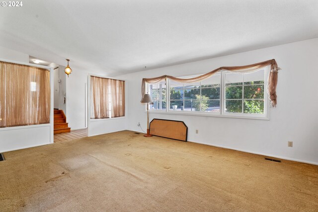 unfurnished living room with light carpet, lofted ceiling with beams, a wood stove, and a textured ceiling