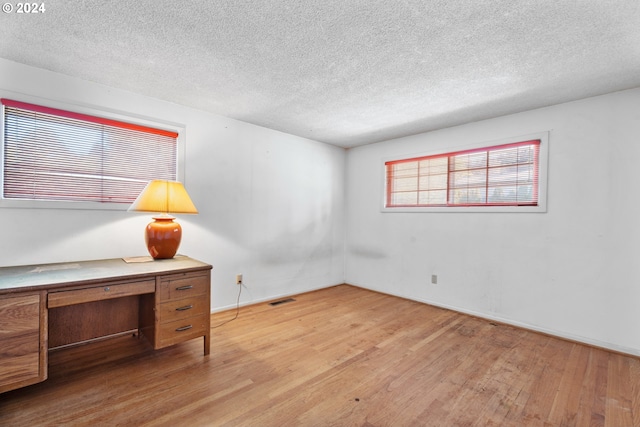 empty room with a textured ceiling, a wealth of natural light, and light wood-type flooring