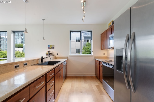 kitchen with light wood-type flooring, light stone counters, stainless steel appliances, sink, and decorative light fixtures