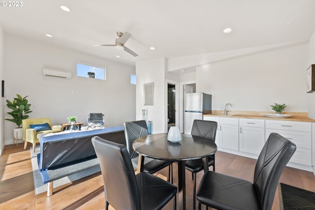 dining area featuring a wall mounted air conditioner, sink, ceiling fan, and light wood-type flooring