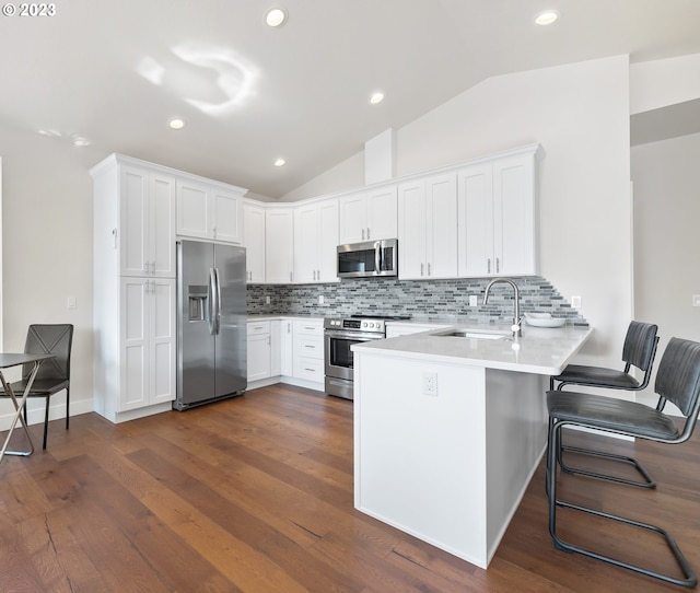 kitchen featuring a kitchen breakfast bar, stainless steel appliances, white cabinetry, lofted ceiling, and backsplash