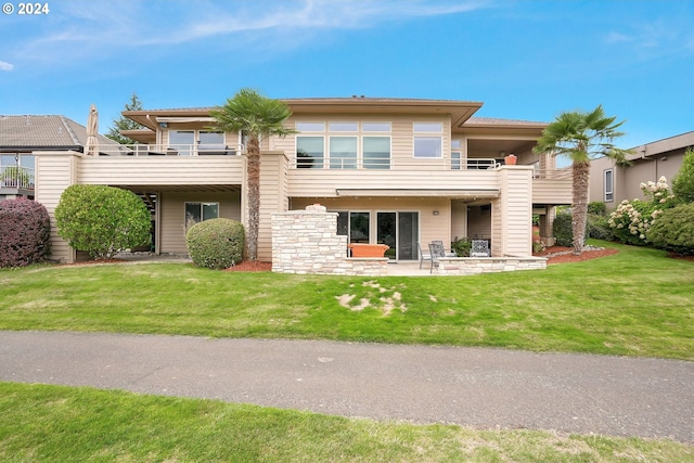 back of property with a balcony, a patio area, and a lawn