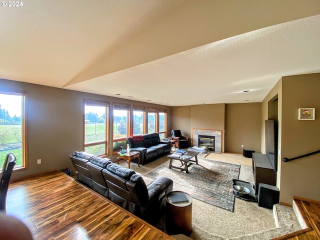 living room with lofted ceiling, a tile fireplace, hardwood / wood-style floors, and a healthy amount of sunlight