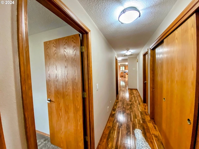 corridor featuring a textured ceiling and dark hardwood / wood-style flooring